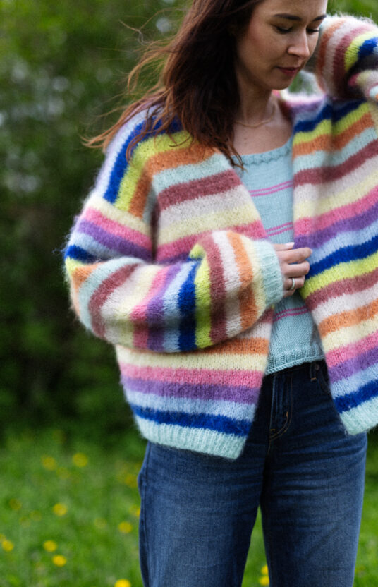 Woman wearing a fluffy rainbow striped cardigan outdoors in a park.