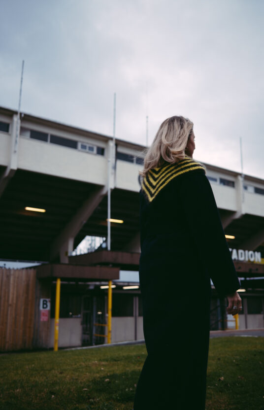 Person wearing a black knitting pattern Glimt shawl / scarf. Knit football team colors. Shawl knitted in Glimt football colors Aspmyra knitting pattern league triangle scarf in Bodø Glimt colors
