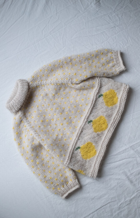Light gray knitted baby sweater with yellow dotted pattern and lemon motifs along the side.